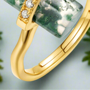 Gold ring with green gemstone and diamonds on a light gray background