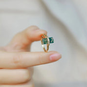 Gold ring with green gemstone on a finger, blurred background