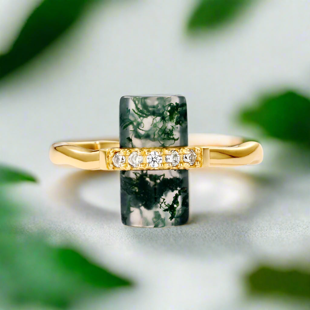 Gold ring with green stone and diamonds on a light gray background