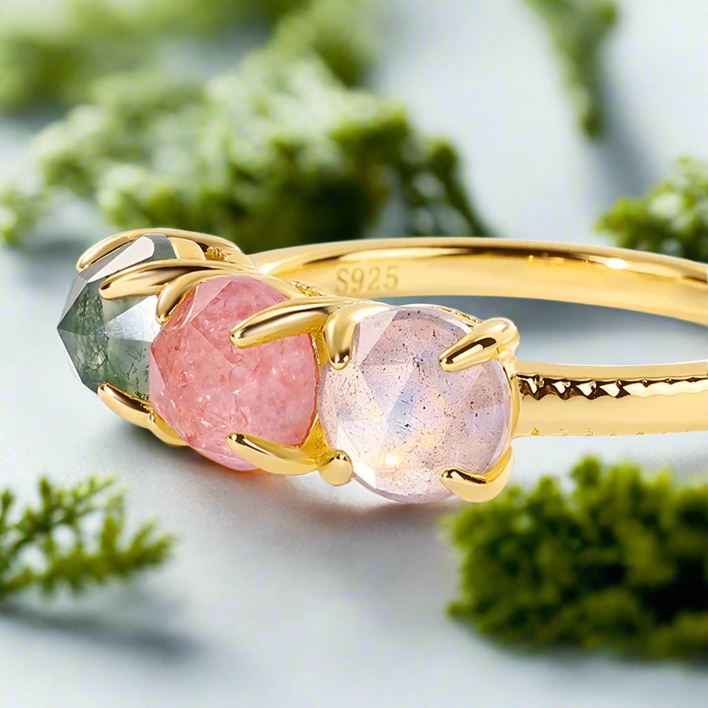 Gold ring with pink and green gemstones on a white background