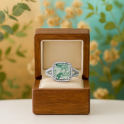 Green gemstone ring in a wooden box with a floral background