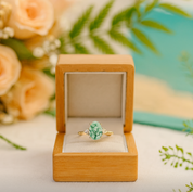 Green gemstone ring in a wooden box with flowers in the background