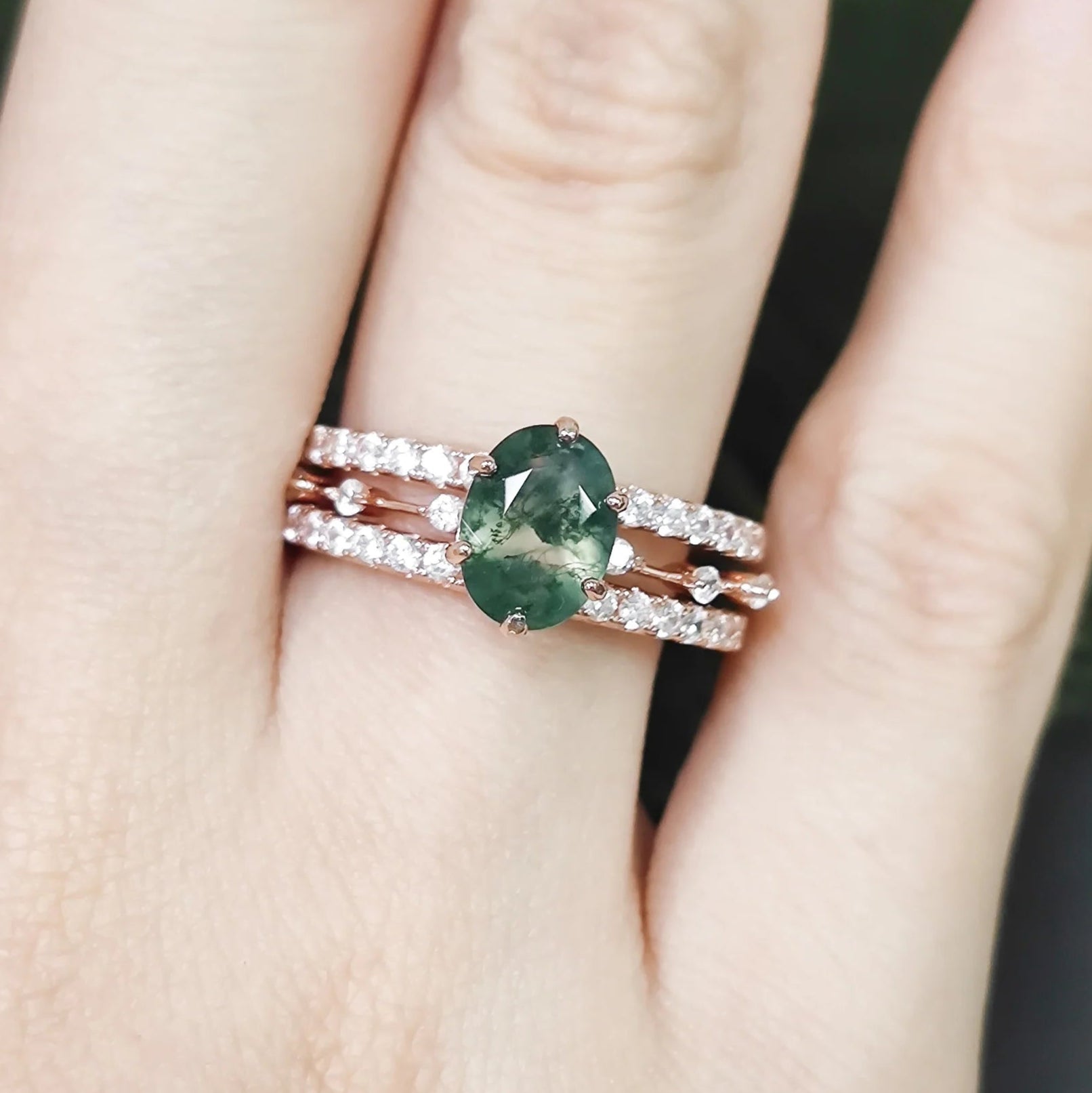 Green gemstone ring with rose gold band on a hand against a blurred natural background