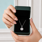 Hand holding a diamond necklace in an open green jewelry box against a light background