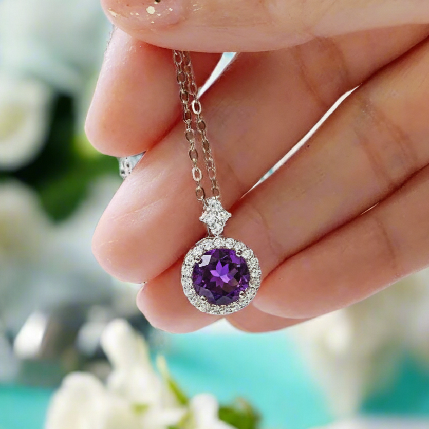 Hand holding a necklace with an amethyst pendant against a floral background