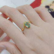 Hand wearing a gold ring with a green gemstone on a blurred background