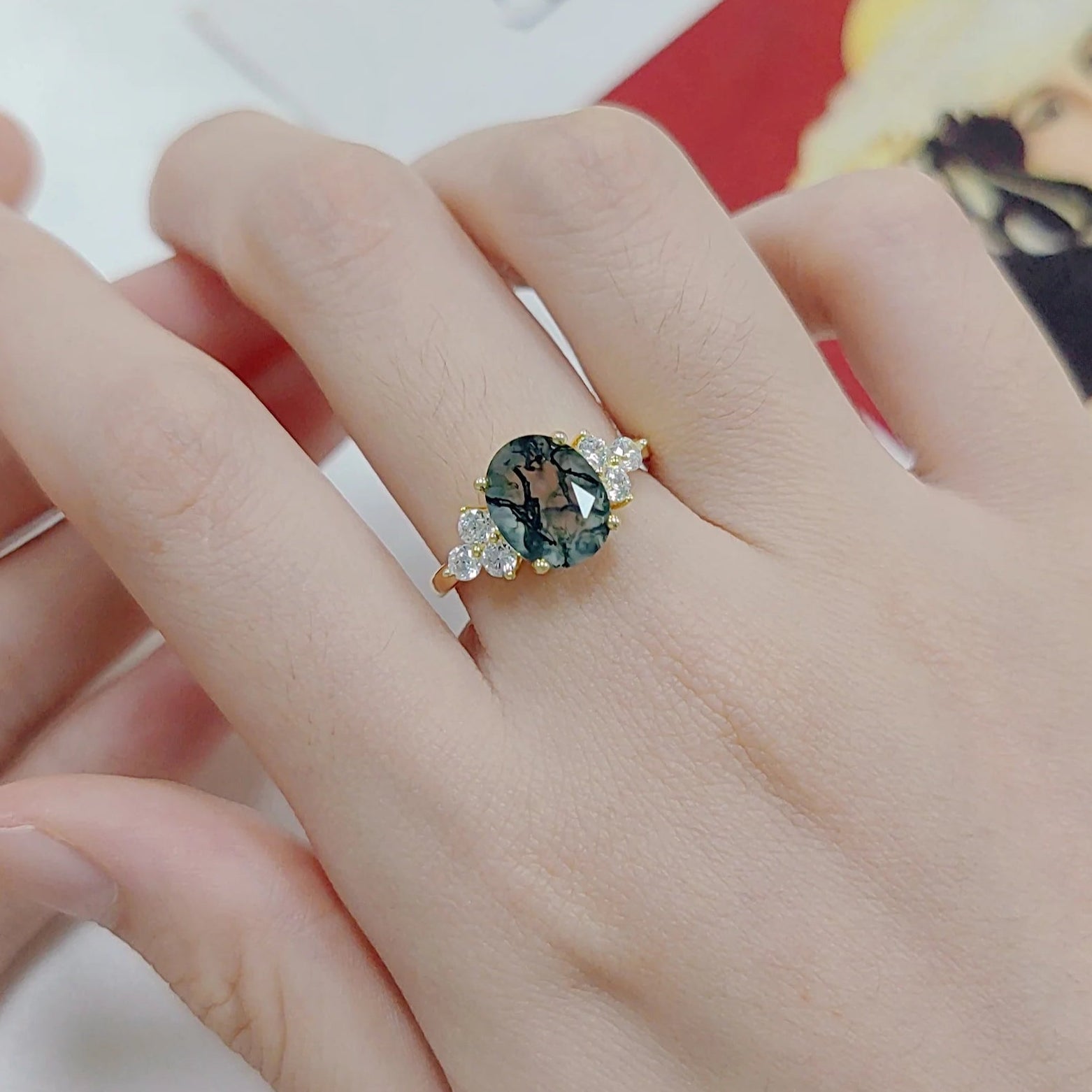 Hand wearing a ring with a green gemstone on a Matisse product background