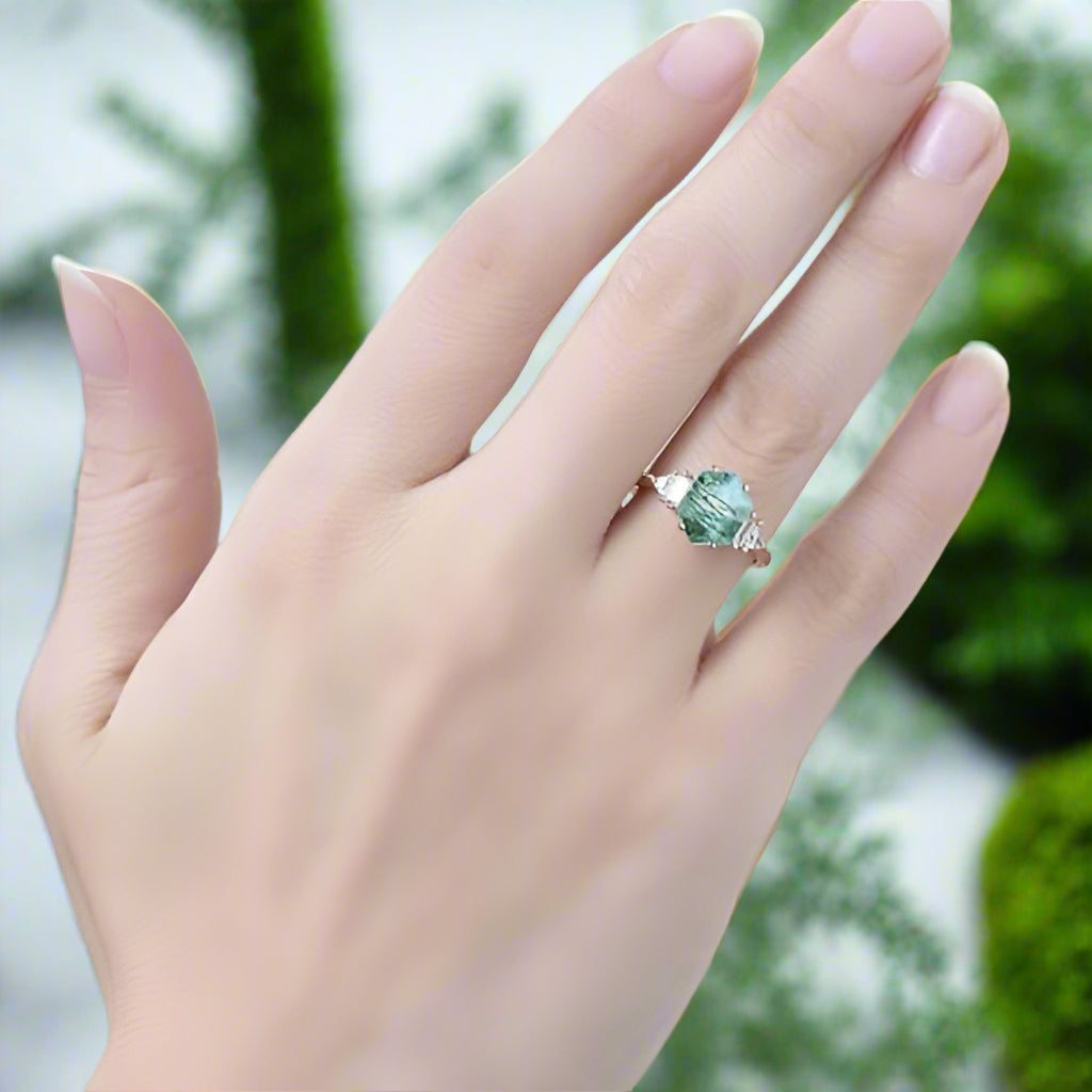 Hand wearing a ring with a green gemstone on a blurred background