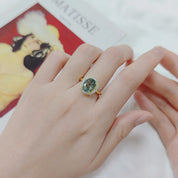 Hand wearing a ring with a green gemstone on a blurred background