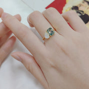 Hand wearing a ring with a green gemstone on a white surface