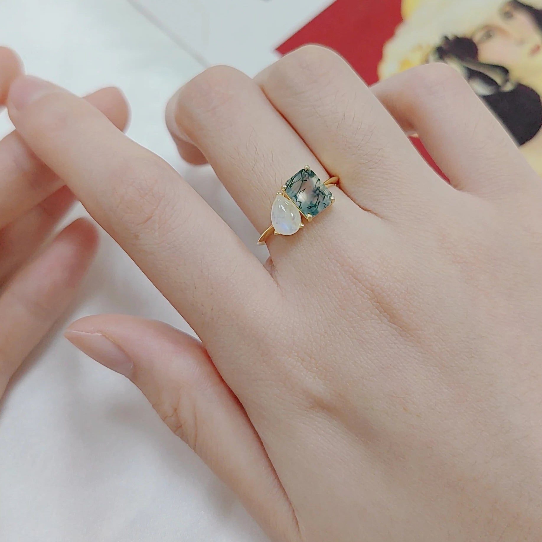Hand wearing a ring with a green gemstone on a white surface