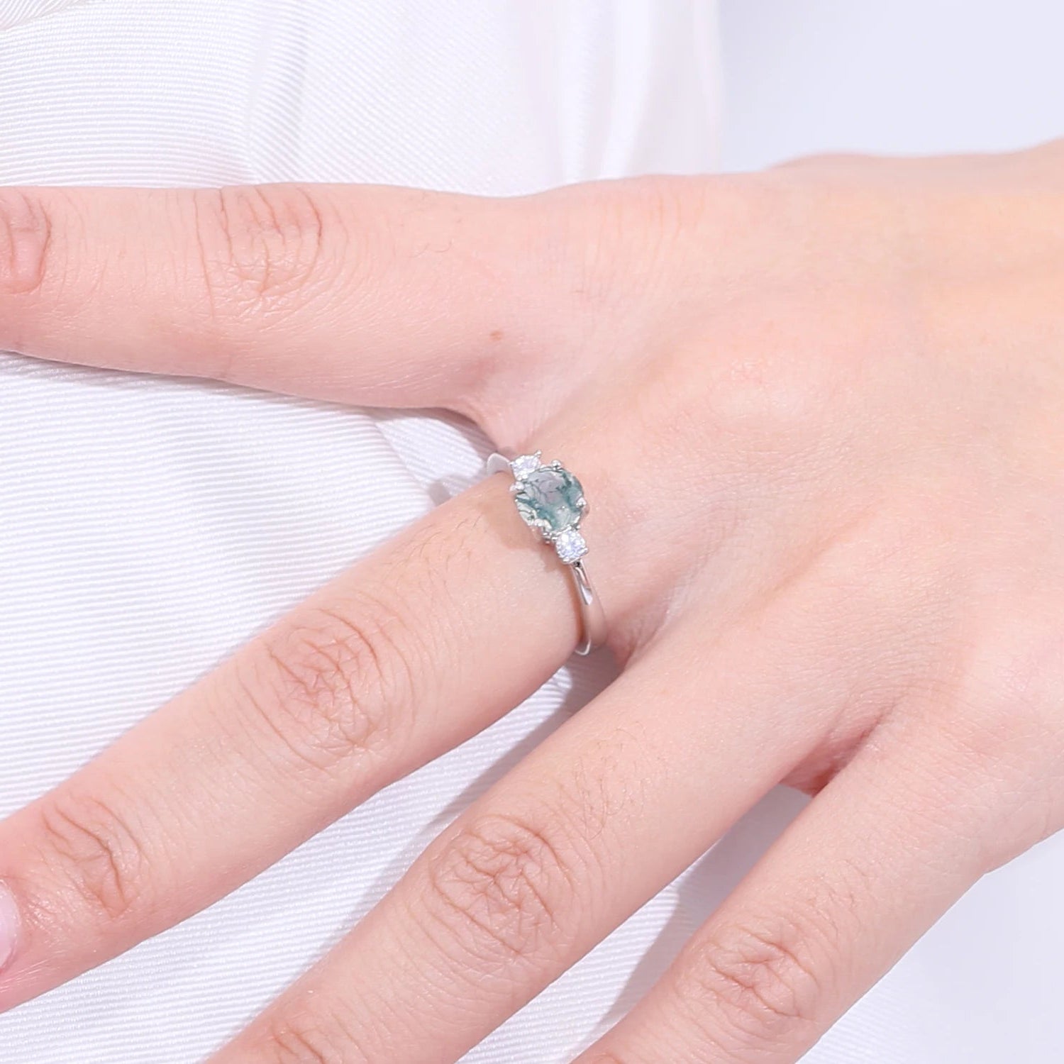 Hand wearing a ring with a heart-shaped gemstone on a white background