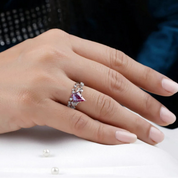 Hand wearing a ring with a pink gemstone on a white surface