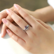 Hand wearing a ring with a purple gemstone on a blurred background
