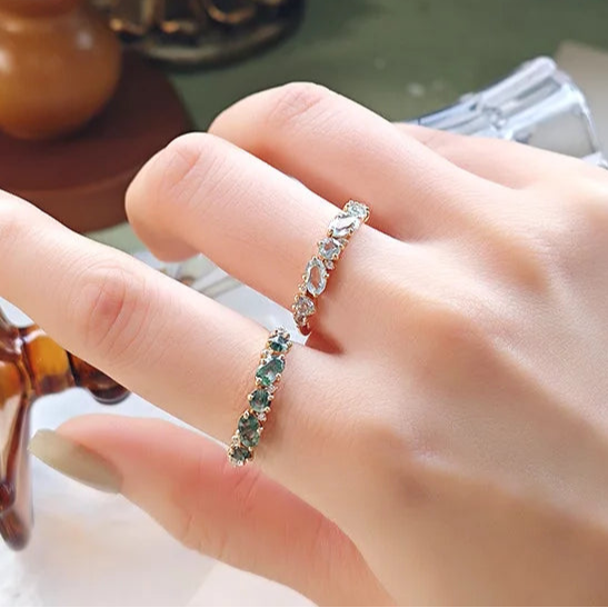 Hand wearing a ring with green gemstones on a blurred background