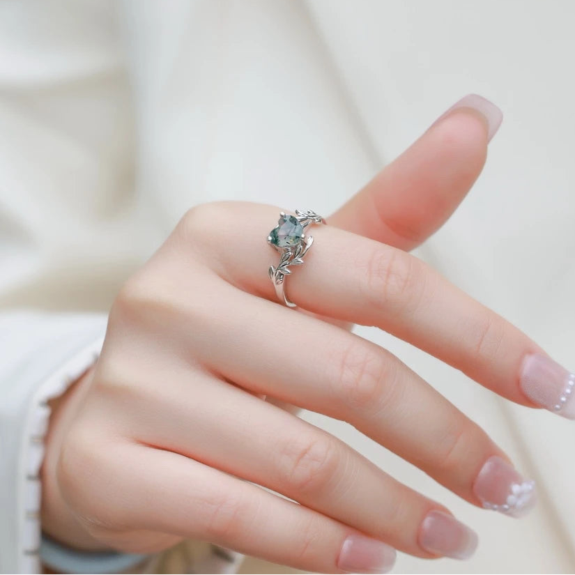 Hand wearing a silver ring with a green gemstone on a light background