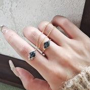 Hand wearing two gold rings with gemstones on a neutral background