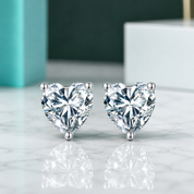 Heart-shaped diamond earrings on a reflective surface with a blurred background