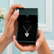 Heart-shaped diamond necklace in a black jewelry box held by hands with light pink nail polish.