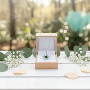 Jewelry box with a necklace featuring a green gemstone, surrounded by greenery and flowers.