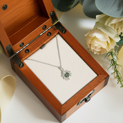 Jewelry box with a necklace featuring a green stone and silver chain, surrounded by flowers.