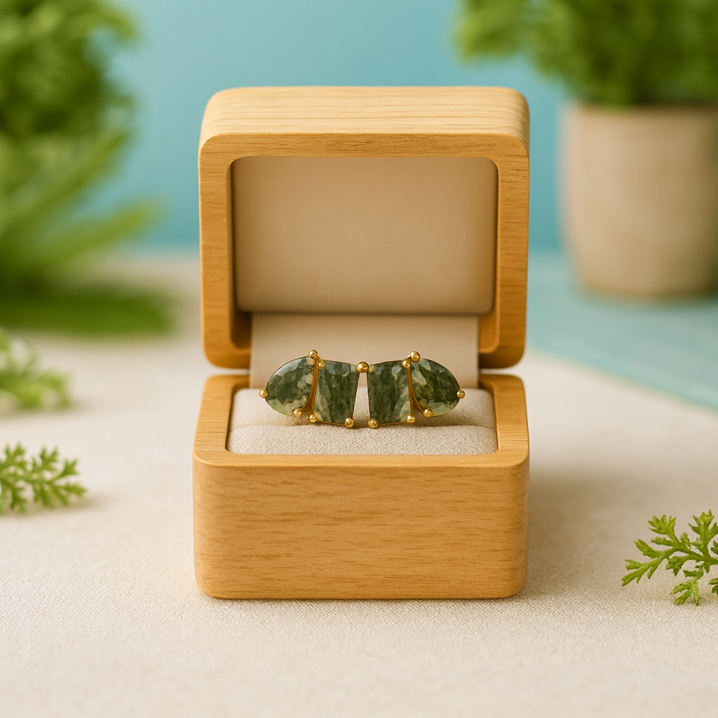Jewelry box with green gemstone earrings on a light surface with plants in the background
