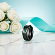 Black ring with green inlay on a light blue and white marble surface