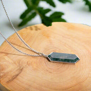 Necklace with a green pendant on a wooden surface with a plant in the background