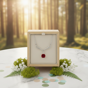 Necklace with a red gemstone in a wooden box against a forest background