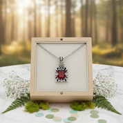 Necklace with a red gemstone in a wooden box against a forest background