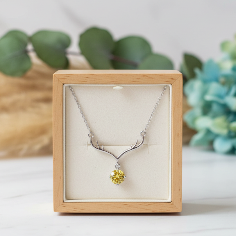 Necklace with a yellow pendant in a wooden box on a white surface with greenery in the background