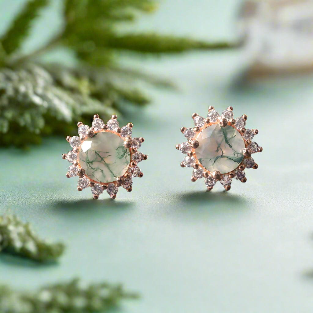 Pair of earrings with green gemstones and rose gold accents on a dark surface