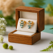 Pair of gold and green earrings in a wooden box with a natural background