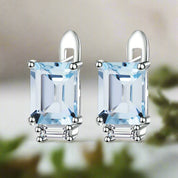 Pair of silver earrings with rectangular blue gemstones on a white background