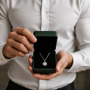Person holding a green jewelry box with a silver necklace featuring a circular pendant.