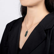 Person wearing a necklace with a green pendant on a plain background