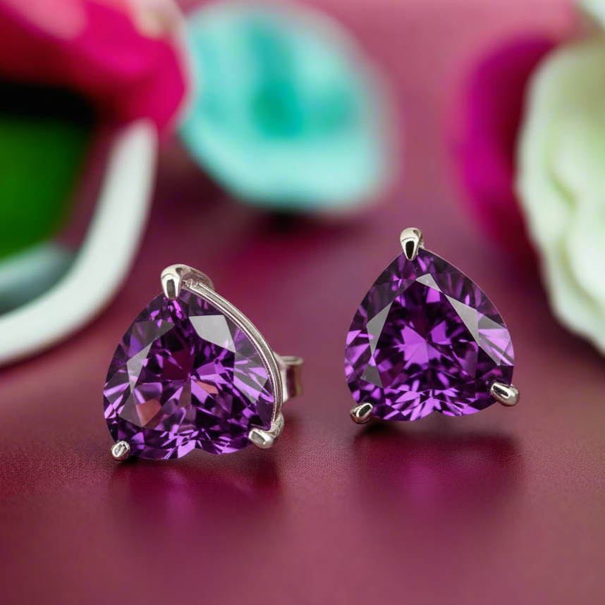 Purple heart-shaped earrings on a reflective surface with flowers in the background