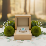 Ring with a blue gemstone in a wooden box surrounded by greenery and flowers.