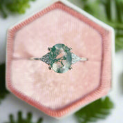 Ring with a green gemstone and diamond accents on a pink fabric background