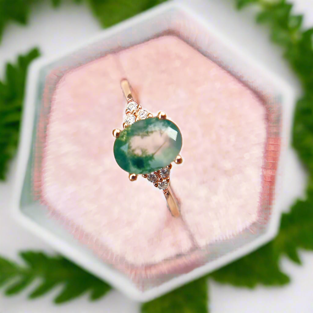 Ring with a green gemstone and rose gold setting on a pink heart-shaped stand.
