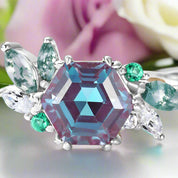 Ring with a large multicolored gemstone and smaller green and clear stones on a white background