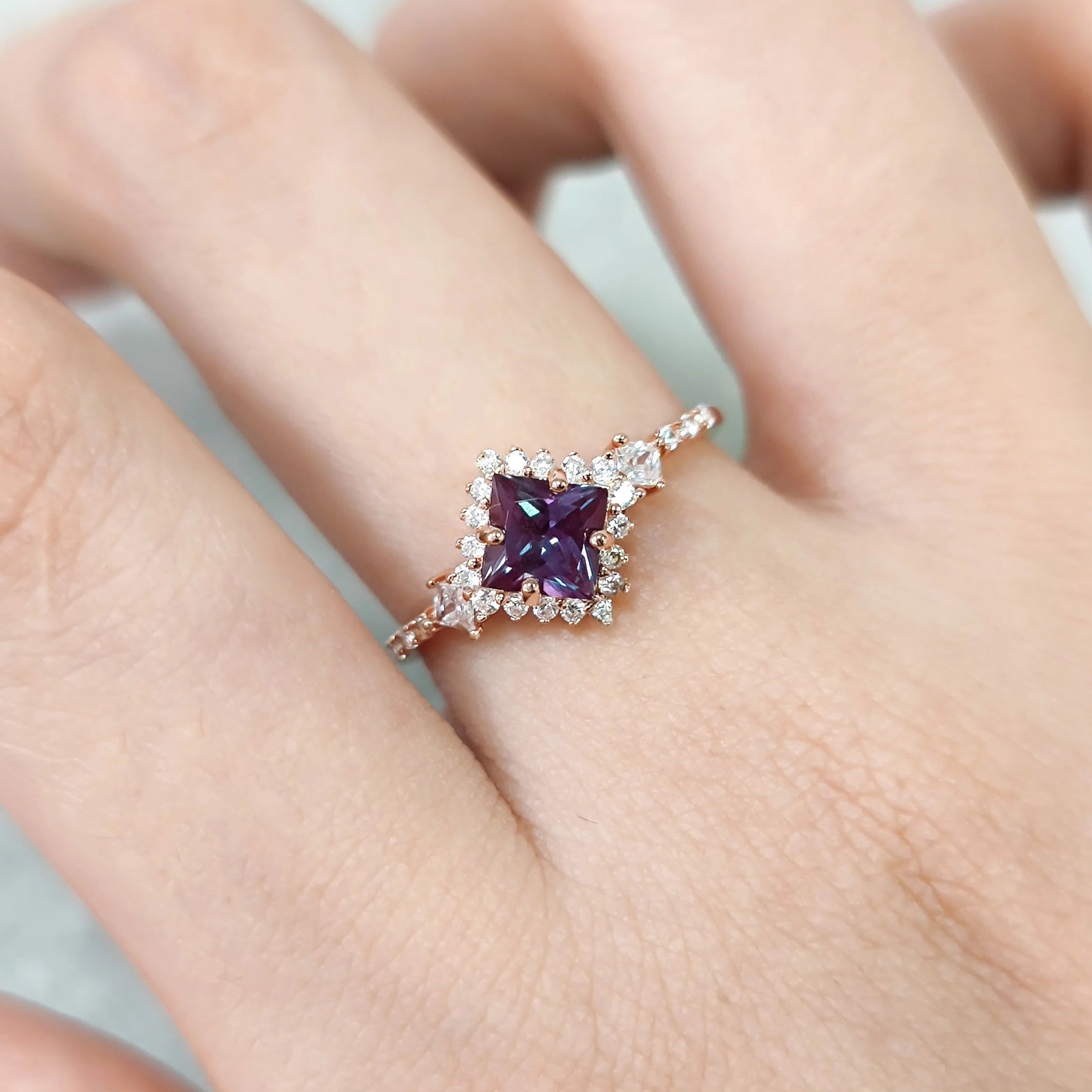 Ring with a purple gemstone on a finger against a neutral background