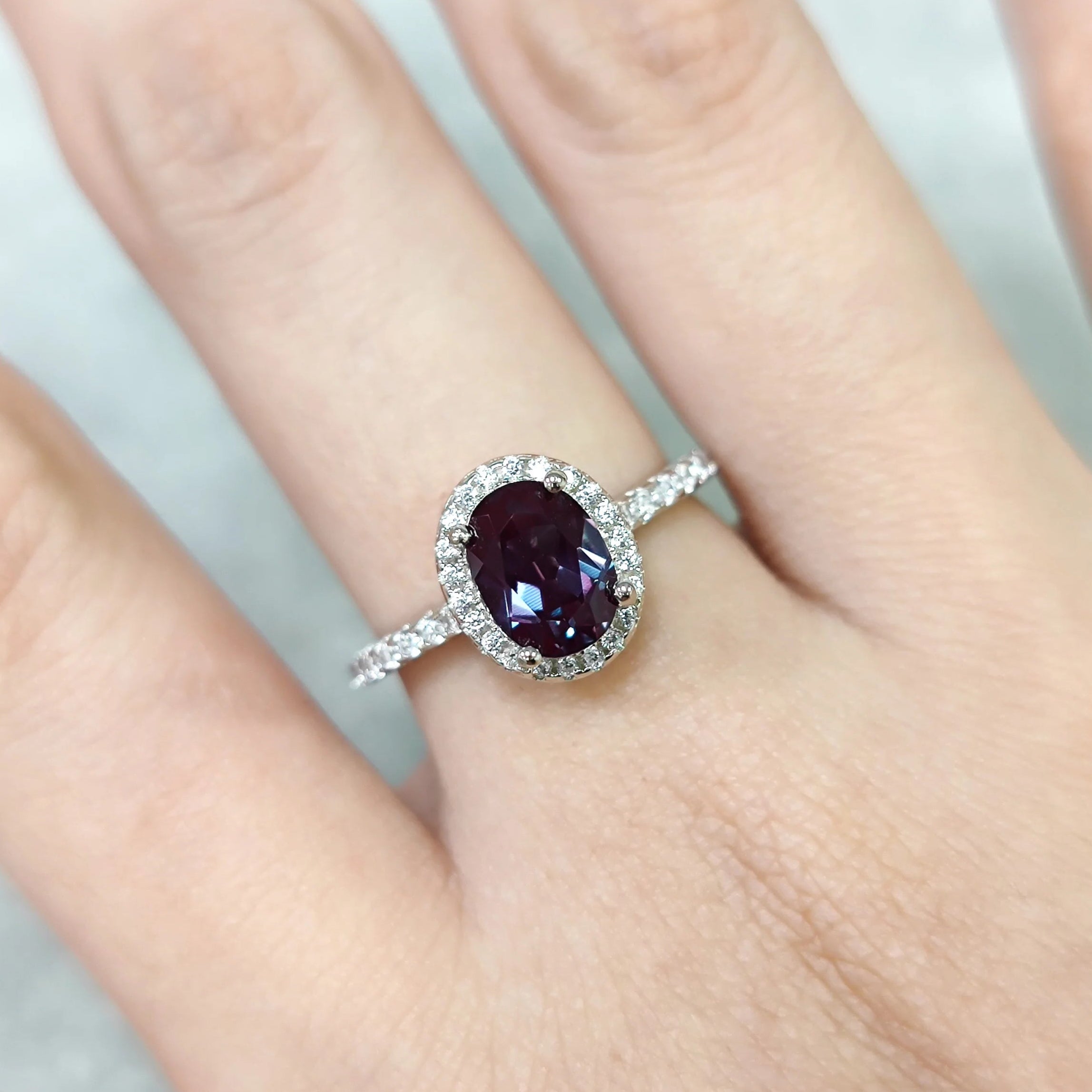 Ring with a purple gemstone on a person's finger against a neutral background