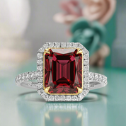 Ring with a red gemstone and diamond accents on a reflective surface