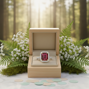 Ring with a red gemstone in a wooden box on a table with flowers and greenery in the background