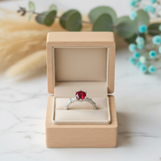 Ring with a red gemstone in an open wooden box on a light surface with decorative elements.