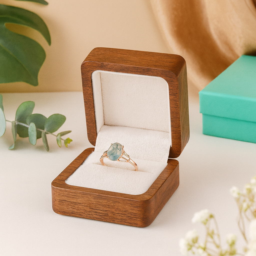 Ring with green gemstone in a wooden box on a light surface with plants in the background