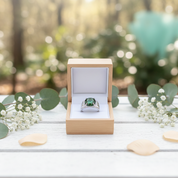 Ring with green gemstone in a wooden box on a wooden surface with blurred natural background