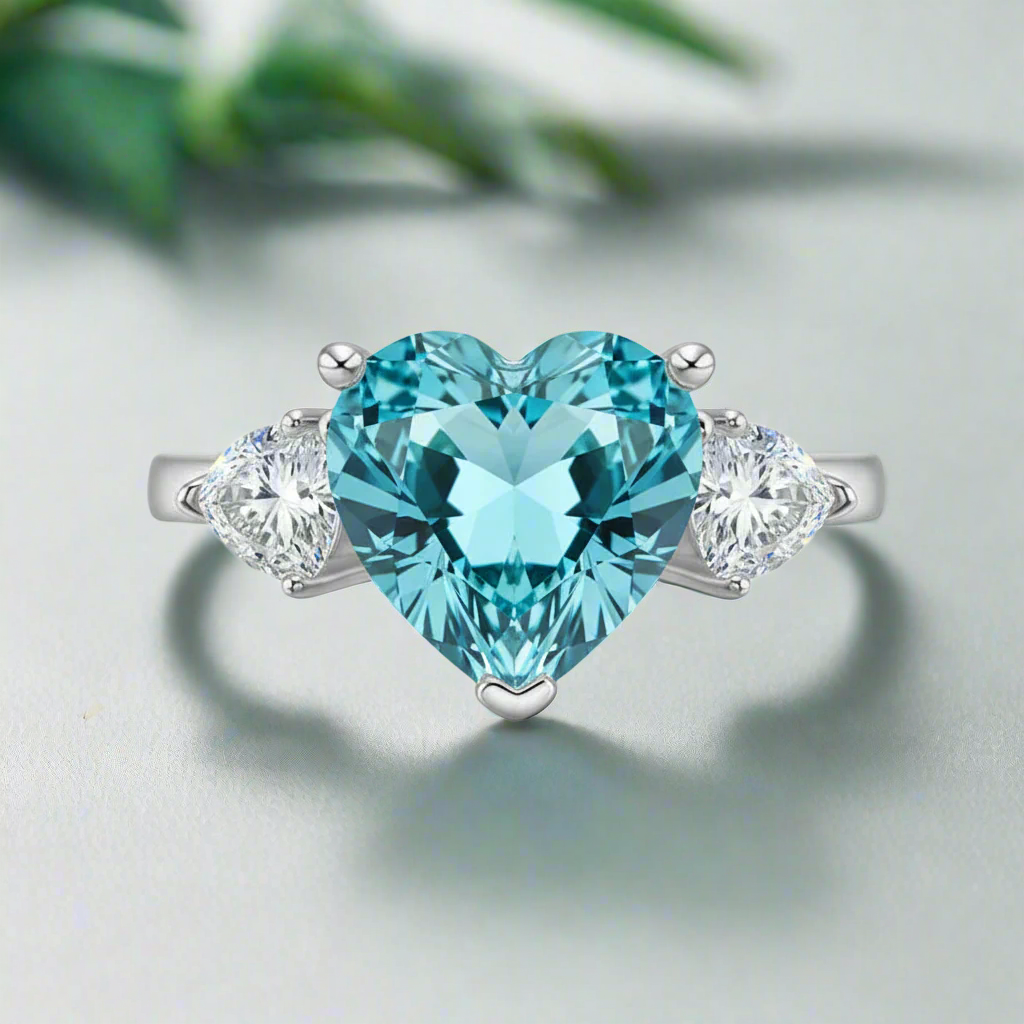Ring with heart-shaped blue gemstone and smaller clear stones on a white background