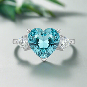 Ring with heart-shaped blue gemstone and smaller clear stones on a white background
